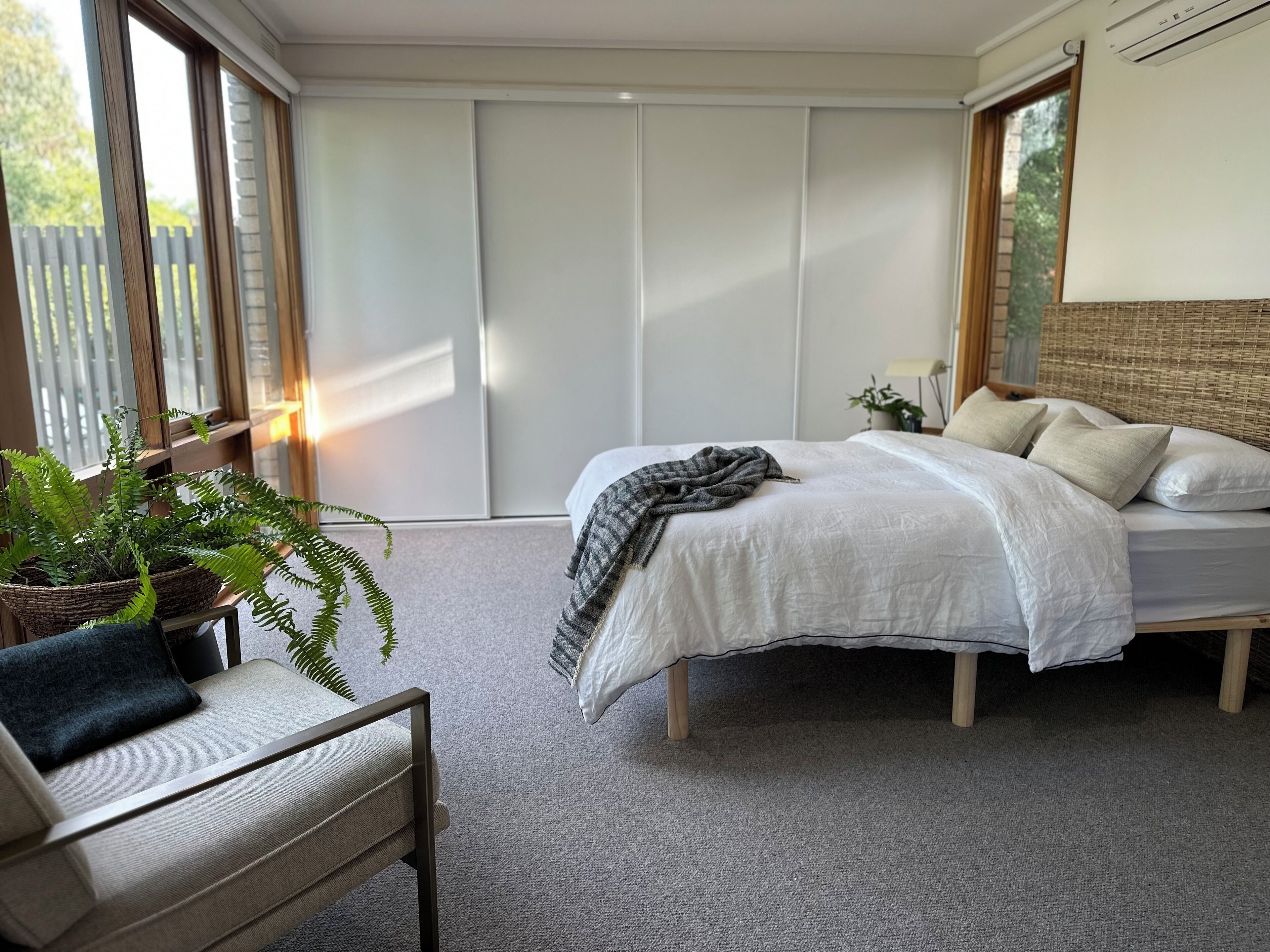 Ein Schlafzimmer mit Bett, einem Sessel, einer Topfpflanze und einer Schiebetür.