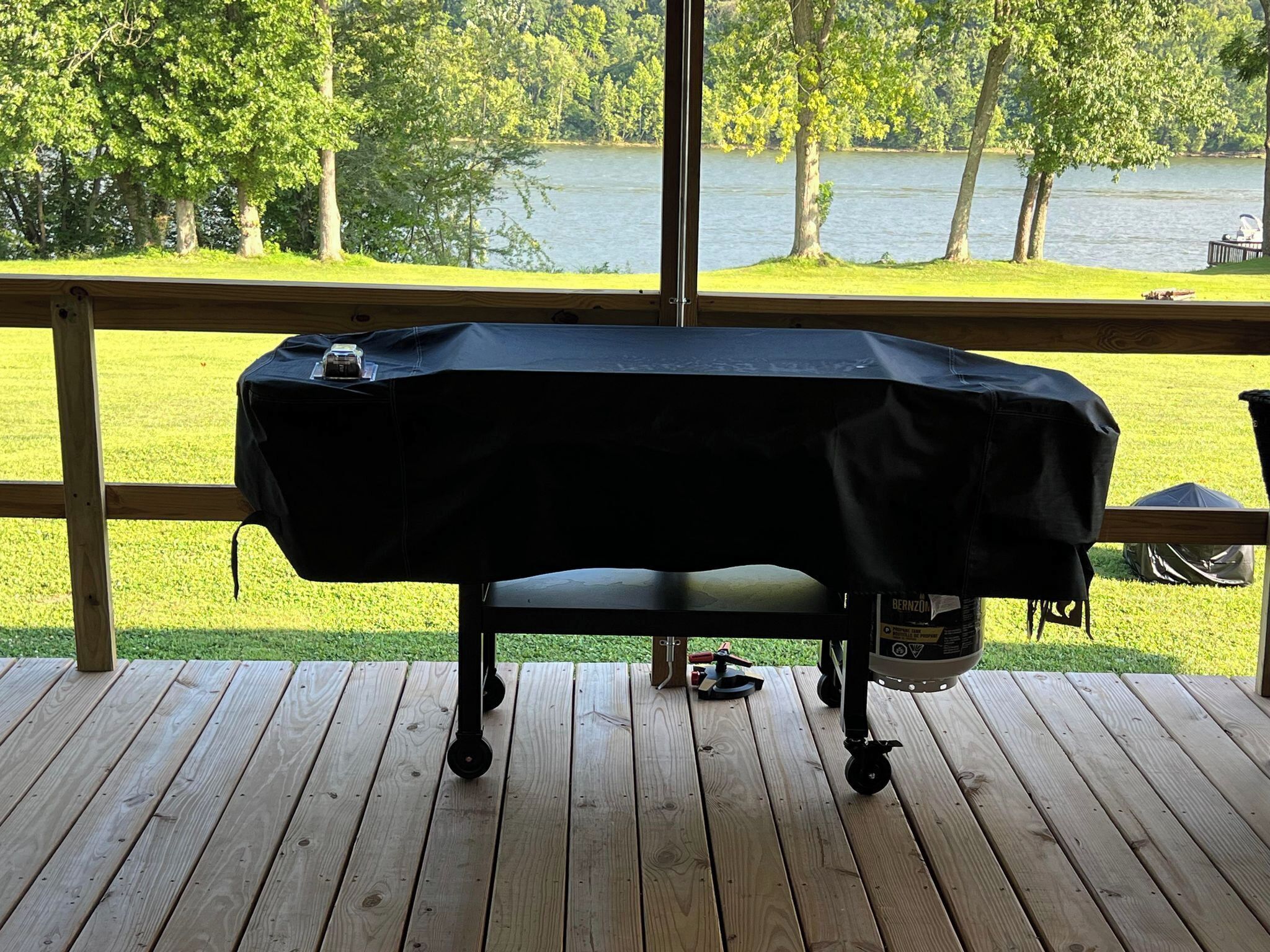 Una parrilla cubierta en una terraza de madera con vista a un lago y árboles.