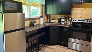 Una cocina equipada con refrigerador, estufa, pileta y taburetes de bar.