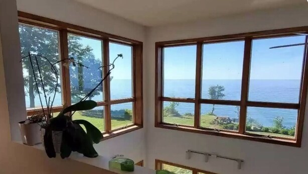 A room with large windows overlooking a body of water and greenery. - Lakeside Resort Home: Sunsets, fishing, paddling - pet friendly (Avon Lake)