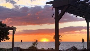 A wooden deck with outdoor seating and a view of the sunset over the ocean. - Lakeside Resort Home: Sunsets, fishing, paddling - pet friendly (Avon Lake)