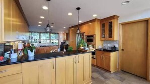 A spacious kitchen with wooden cabinets, a black countertop, and pendant lighting. - Lakeside Resort Home: Sunsets, fishing, paddling - pet friendly (Avon Lake)