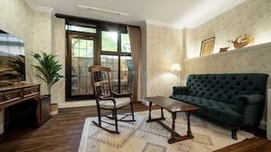 A living room with a dark green sofa, a wooden rocking chair, a wooden coffee table, and a television on a wooden cabinet.