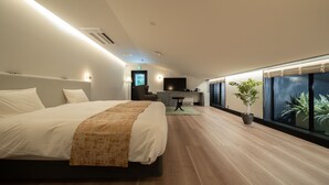 A modern hotel room with a large bed, a small seating area, a TV, and a large window with a view.