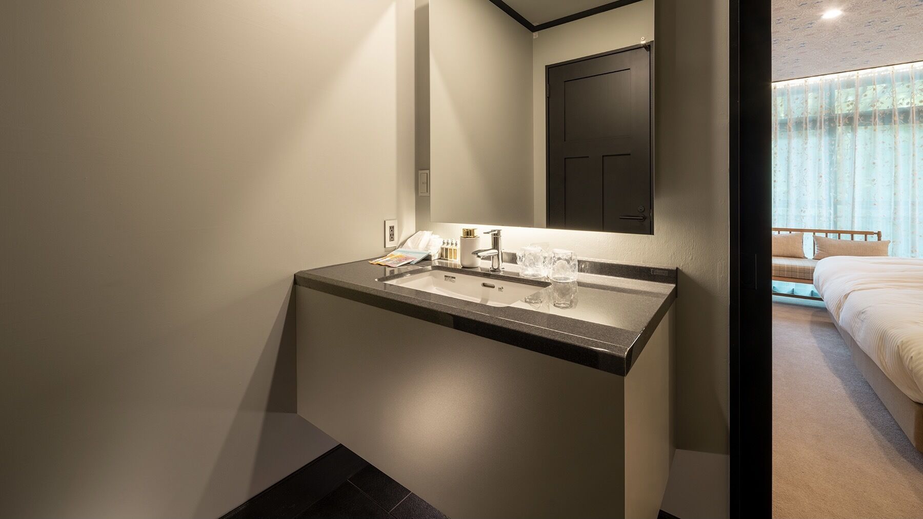 Ein modernes Badezimmer mit Waschbecken, Spiegel und Blick ins Schlafzimmer.