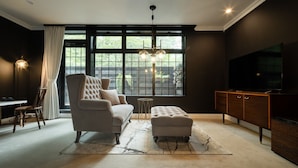 A modern living room with a sofa, ottoman, TV, and a dining area with chairs and a table.