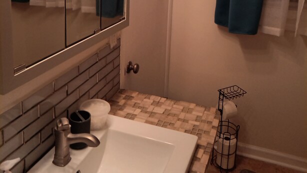 Une salle de bain avec un lavabo blanc, un miroir avec éclairage intégré, un porte-serviettes et un rideau de douche.
