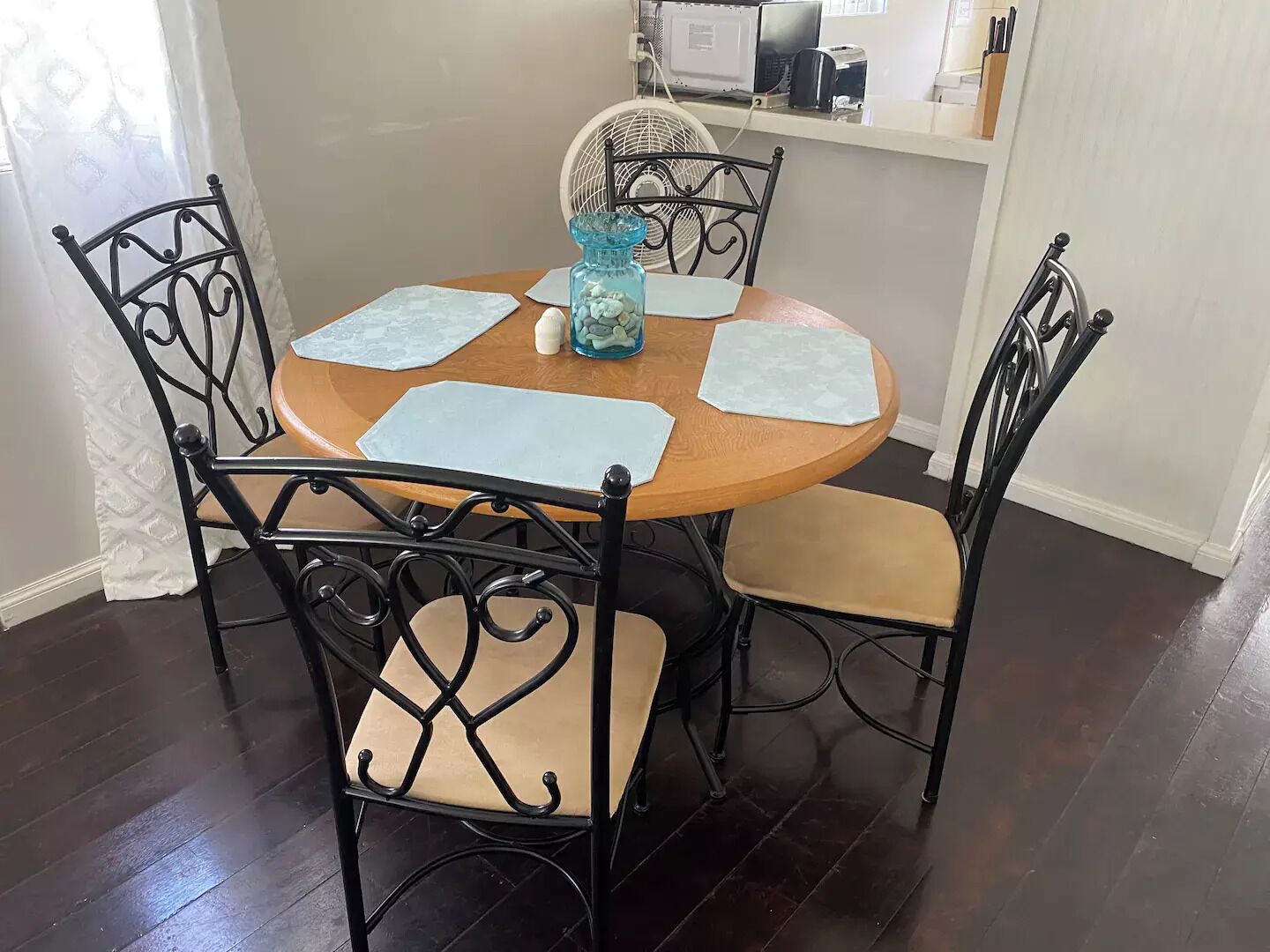 Un comedor con una mesa redonda de madera, cuatro sillas y un ventilador.