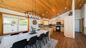 Une cuisine moderne avec des meubles en bois, un grand îlot central et un coin repas comprenant une table blanche et des chaises noires.