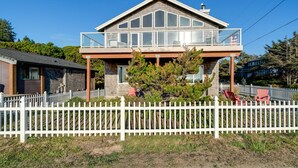 Une maison à deux étages avec un balcon, une clôture en piquets et un petit arbre devant.