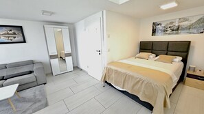 A bedroom with a bed, a grey sofa, a small table, a wardrobe, and a painting on the wall.