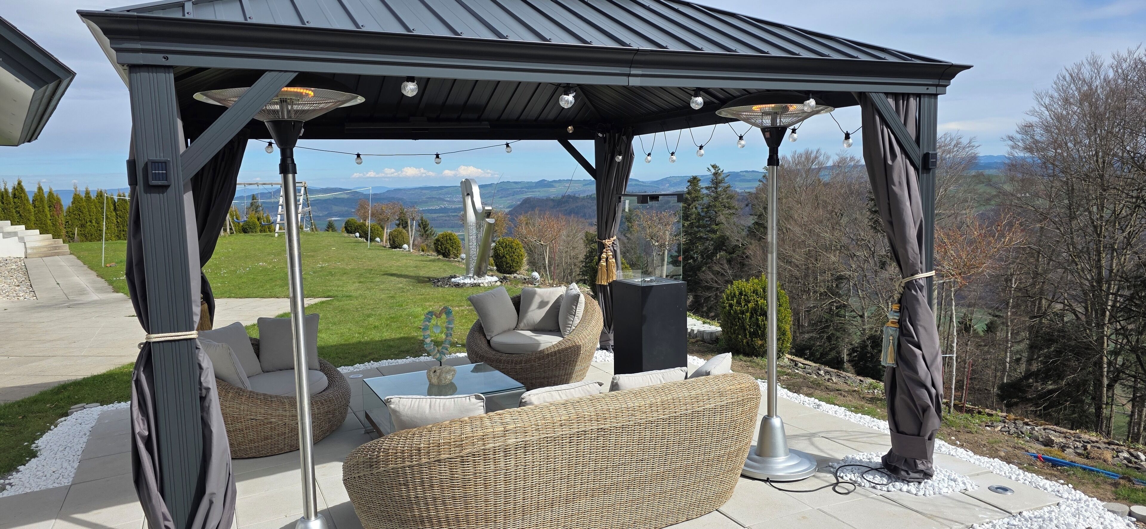 Una terrazza esterna con mobili in vimini, un tavolo con piano in vetro e una pergola decorata con luci a stringa.