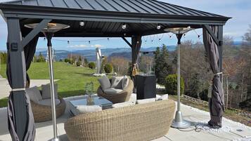 Una terrazza esterna con mobili in vimini, un tavolo con piano in vetro e una pergola decorata con luci a stringa.