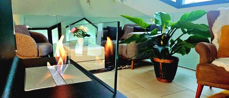 A modern living room with a glass coffee table, two sofas, a potted plant, and a fireplace.