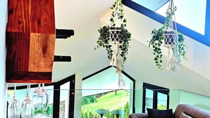 A modern interior with a wooden accent wall, hanging macramé plant hangers, and a view of a green landscape through large windows. - Hilltop Luxury Villa with Minigolf, Indoor Pool, Wellness & Spa (Oberbütschel)