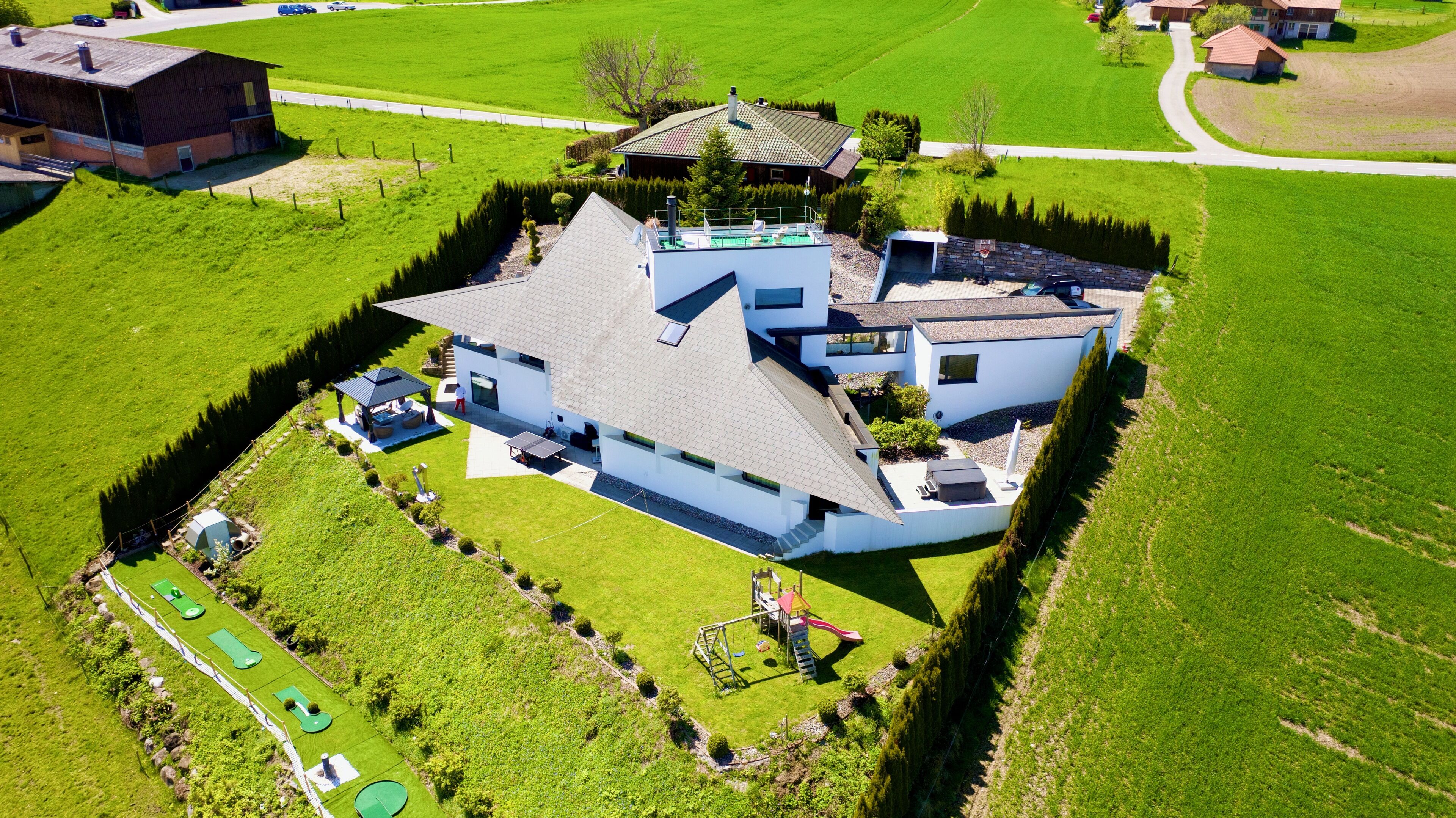 Una casa moderna con un grande prato, un campo da tennis e un'area giochi.