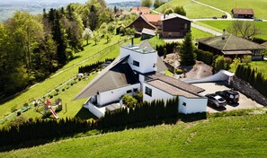 A modern house with a sloped roof, surrounded by lush green fields and trees.