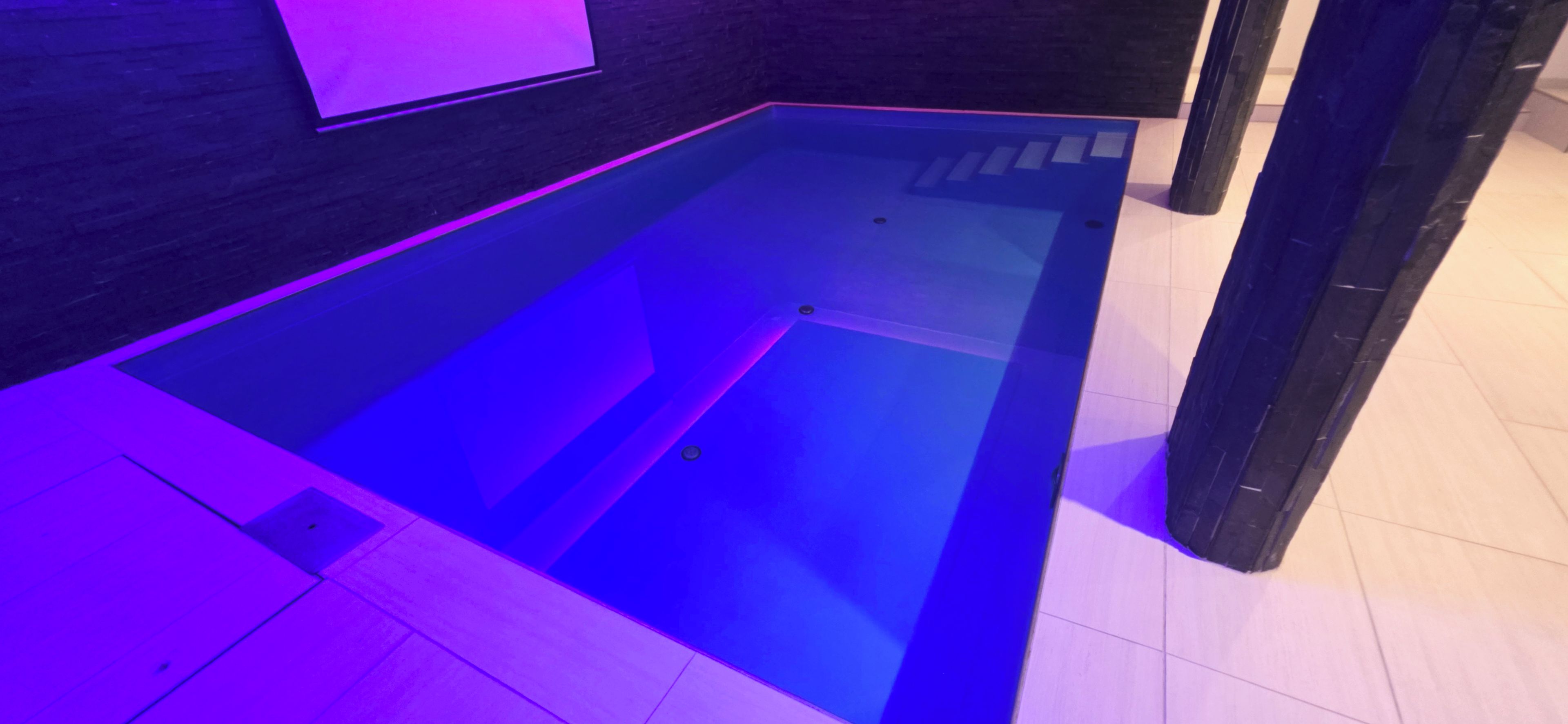 Ein rechteckiger Pool mit dunklem Boden und violetter Beleuchtung.