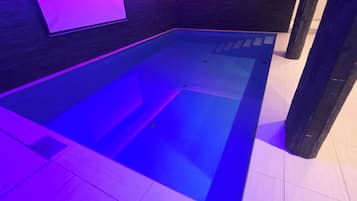 Ein rechteckiger Pool mit dunklem Boden und violetter Beleuchtung.