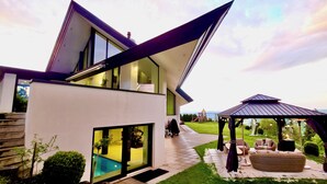 A modern two-story house with a glass-enclosed patio, a swimming pool, and a gazebo. - Hilltop Luxury Villa with Minigolf, Indoor Pool, Wellness & Spa (Oberbütschel)