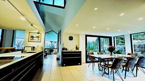 A modern kitchen with a large island, a dining area with a table and chairs, and large windows offering a view of the outdoors.