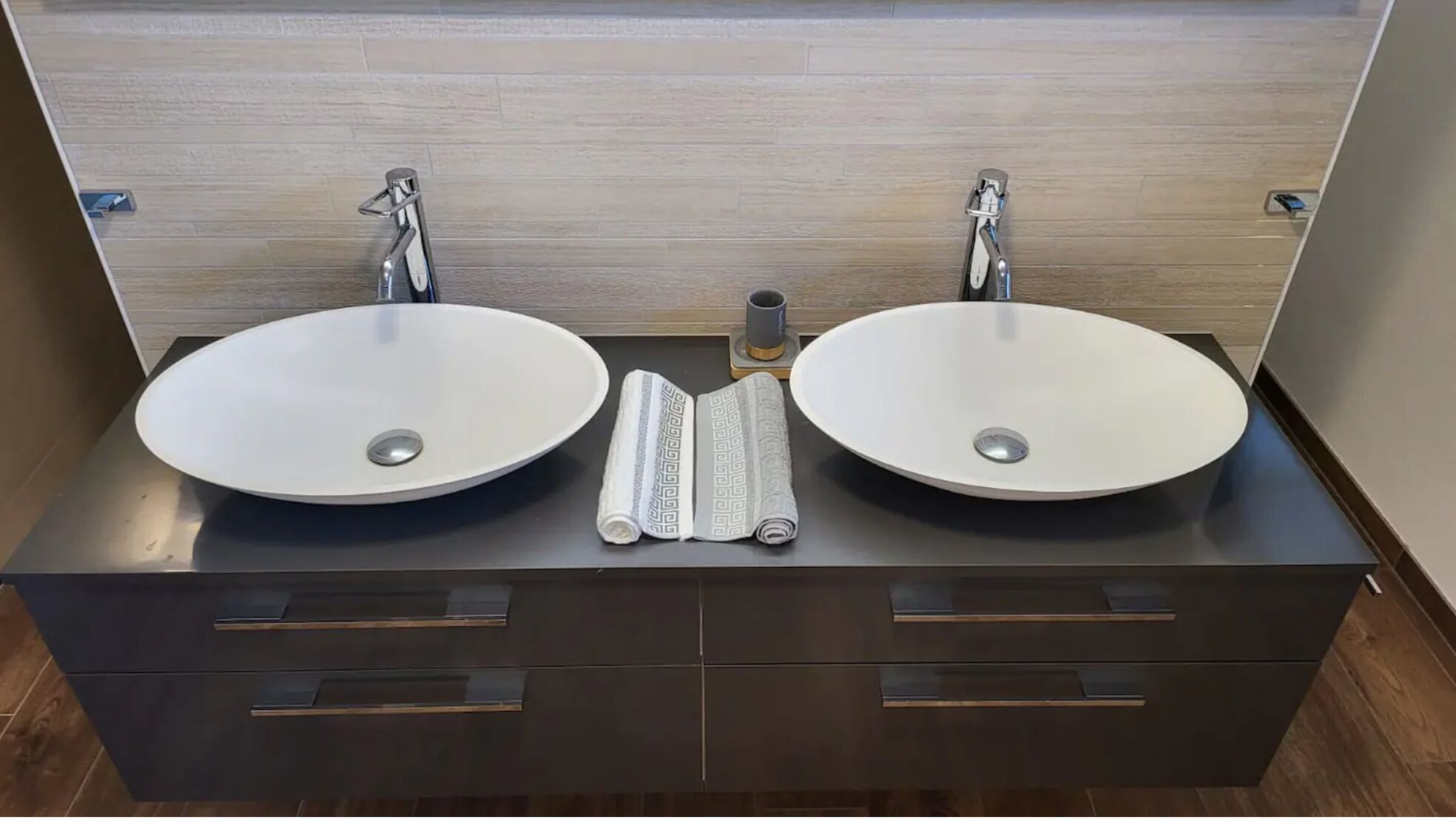 Une salle de bain moderne avec deux vasques rondes blanches, un petit flacon de savon liquide et une serviette à motifs géométriques.