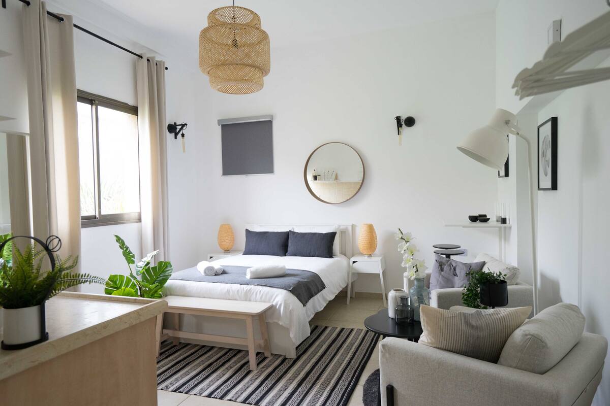 Une chambre à coucher moderne avec un lit, des tables de chevet, un miroir rond et une lampe de chevet.