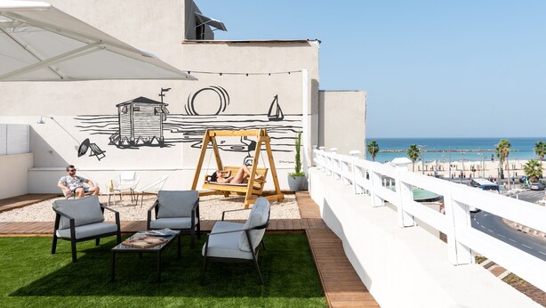 A rooftop terrace with a swing, outdoor seating, and a mural of a sailboat. - YARKON - By Beach Apartments TLV (Tel Aviv)