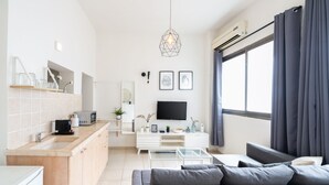 A modern apartment with a kitchen, dining area, and living room. It features a flat-screen TV, a sofa, and a dining table. - YARKON - By Beach Apartments TLV (Tel Aviv)