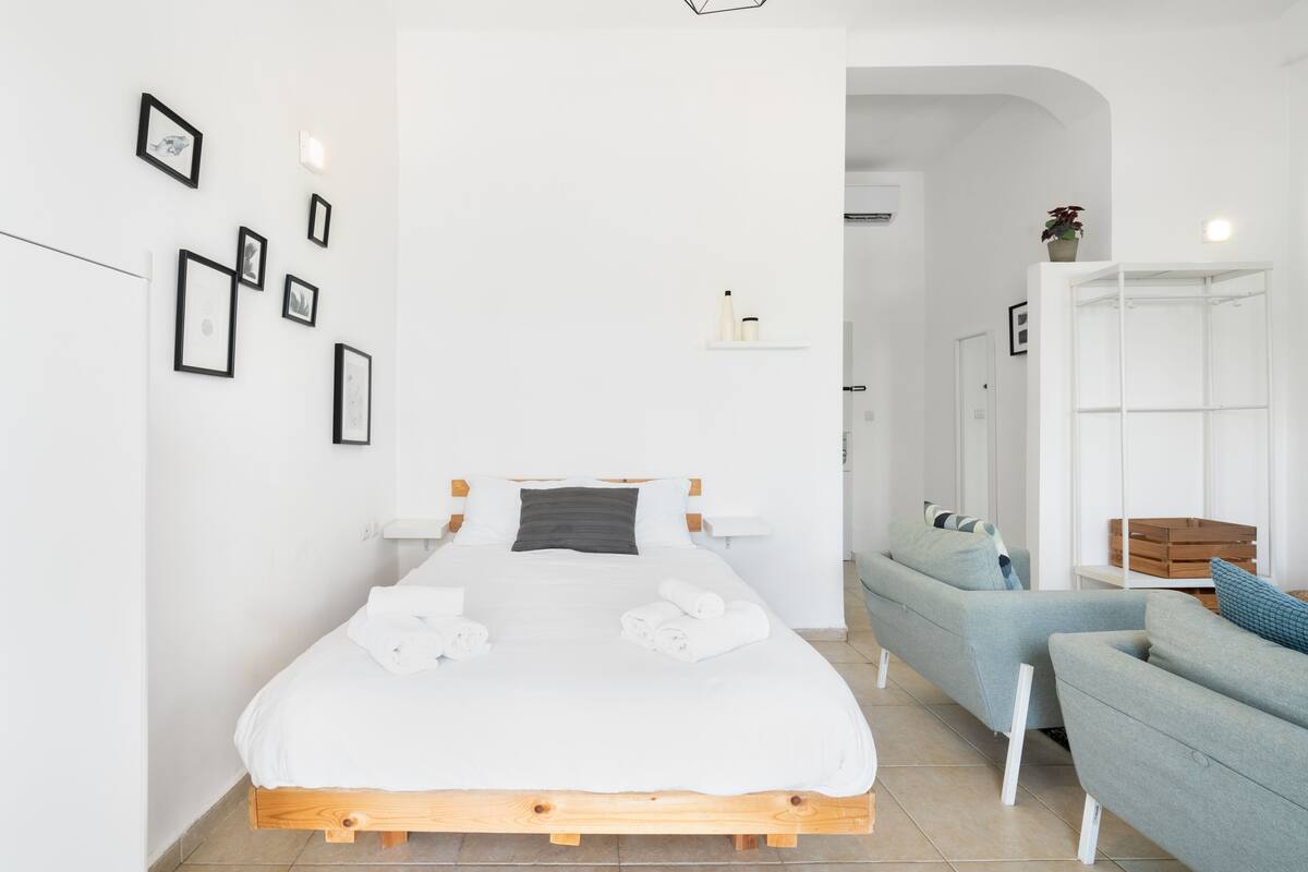 Une chambre à coucher moderne avec un lit en bois, un canapé gris et une armoire blanche.