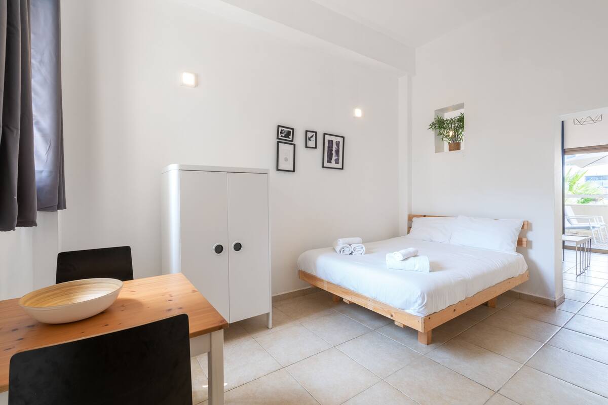 Une chambre à coucher moderne avec un lit en bois, une table à manger avec un saladier, et une armoire blanche.
