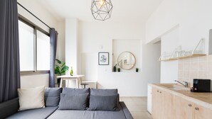 A modern living room with a grey sofa, a glass coffee table, and a kitchen area with wooden cabinets and a countertop. - YARKON - By Beach Apartments TLV (Tel Aviv)