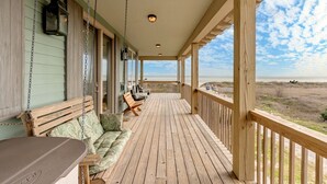 A wooden deck with a view of the beach, a bench, and a table.