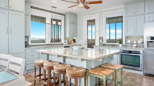 A spacious kitchen with light blue cabinets, a large island with stools, and a ceiling fan.