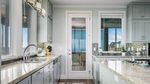 A modern kitchen with granite countertops, white cabinets, and a view through a glass door to the outdoors.