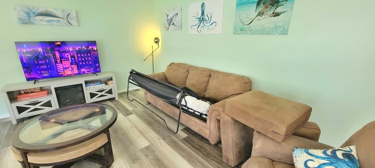 Una sala de estar con un sofá, una mesa de centro de vidrio, un televisor sobre un mueble bajo y obras de arte en las paredes.