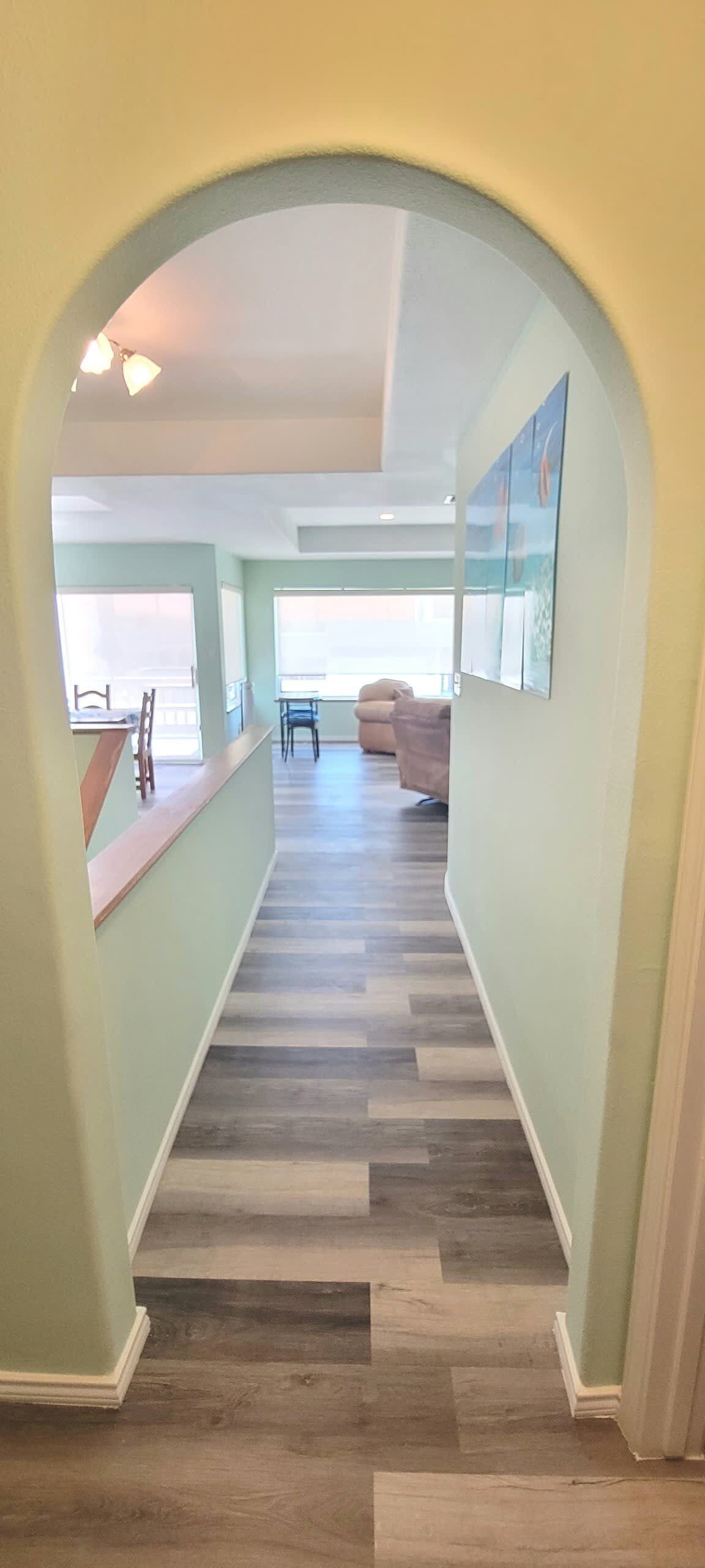 A hallway with a wooden floor, a dining area with a table and chairs, and a living room with a couch.