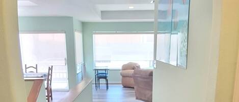 A hallway with a wooden floor, a dining area with a table and chairs, and a living room with a couch.