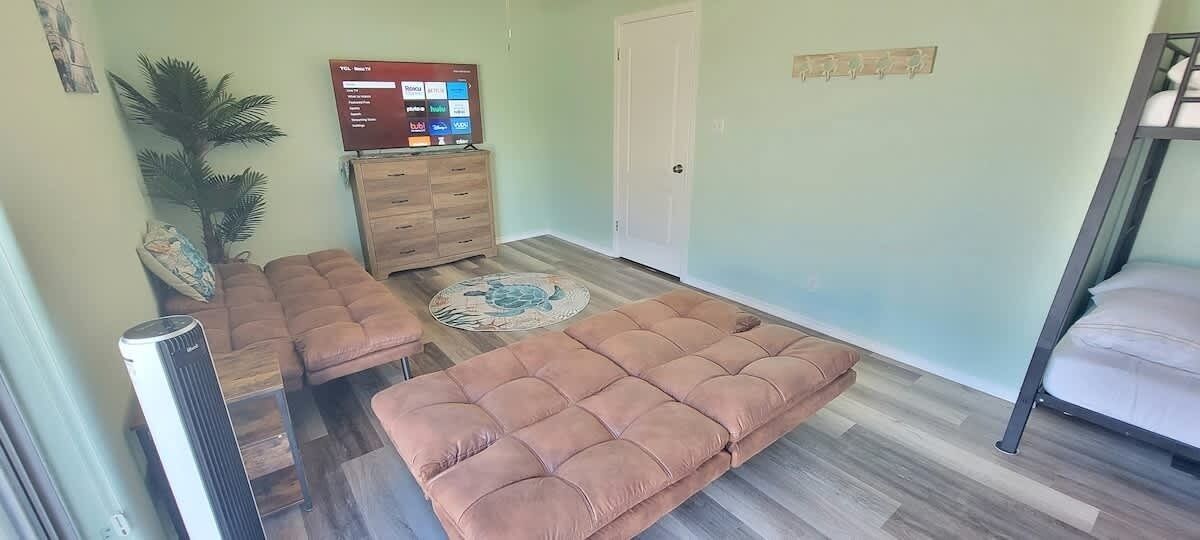 A room with a sofa set, a TV, a wooden cabinet, and a bed.
