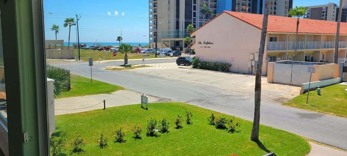 A hotel with a red roof, a sign reading "The Dolphins", and a parking lot with a few cars.