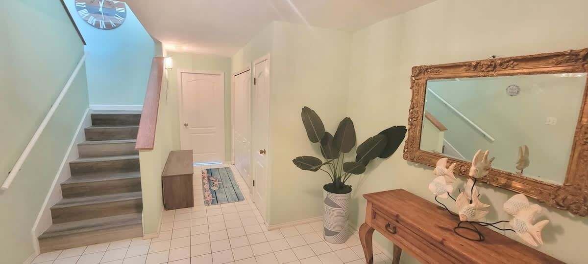 Una escalera que lleva a una puerta, una planta en maceta, un espejo y objetos decorativos sobre una consola de madera.