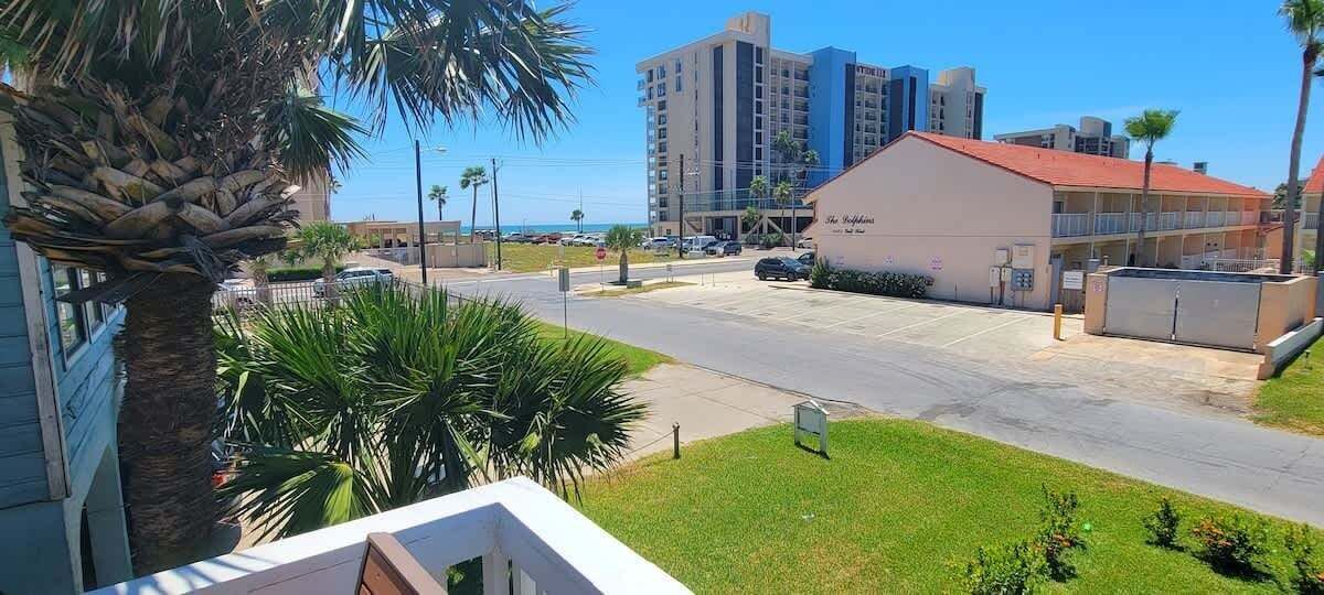 A hotel with a parking lot, a building with a red roof, and palm trees.