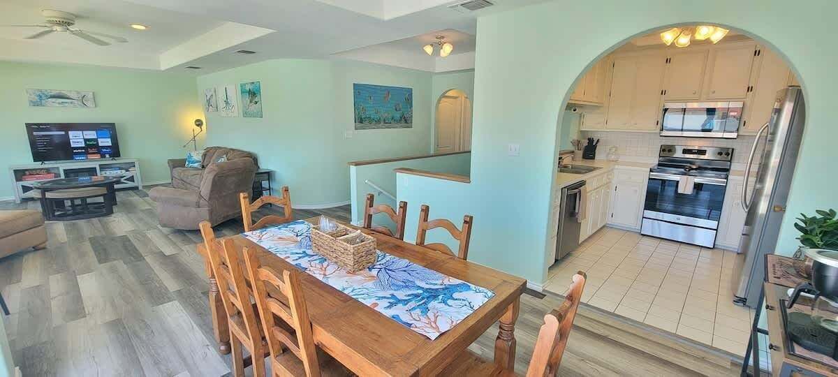 A spacious living area with a dining table, a sofa, and a TV. There is a kitchen with modern appliances and an archway leading to another room.