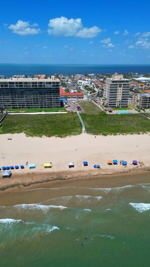Vista aérea de una playa con un hotel, una piscina y una vista despejada del océano.