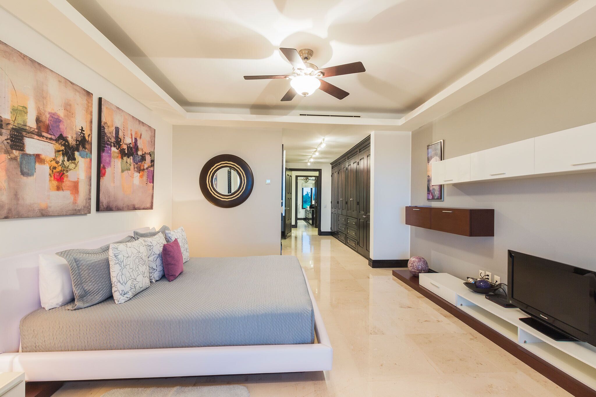 A modern bedroom with a bed, a ceiling fan, artwork on the walls, and a TV on a stand.