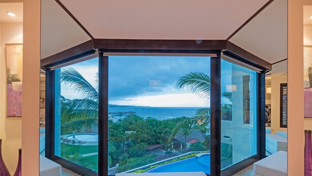 Ein modernes Zimmer mit einem großen Panoramafenster, das einen Blick auf einen Pool und eine tropische Landschaft bietet.