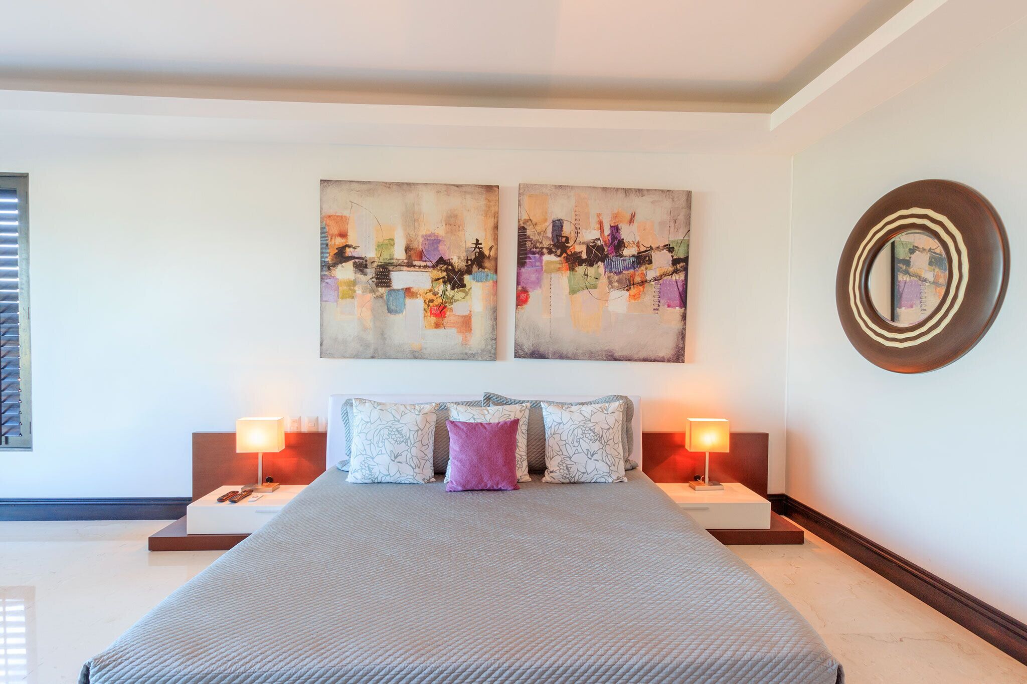 A hotel room with a large bed, two bedside tables, and two wall-mounted paintings.