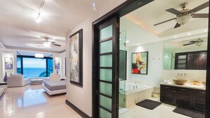 Ein modernes Interieur mit einem Wohnbereich, einer Glastür, die zum Badezimmer führt, und Blick auf den Ozean.