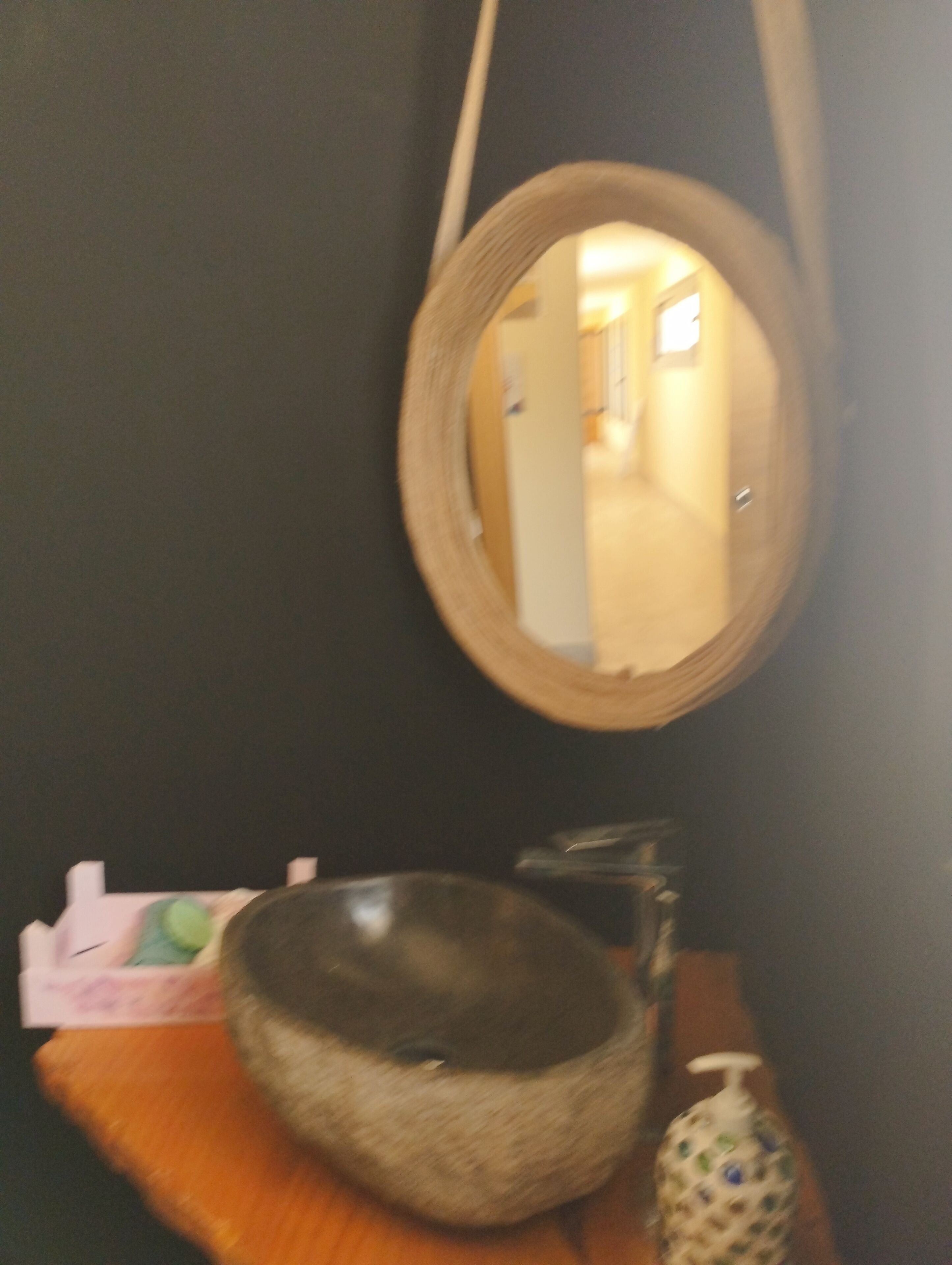 Un baño con un espejo redondo, un lavabo de cesta tejida y un dispensador de jabón.