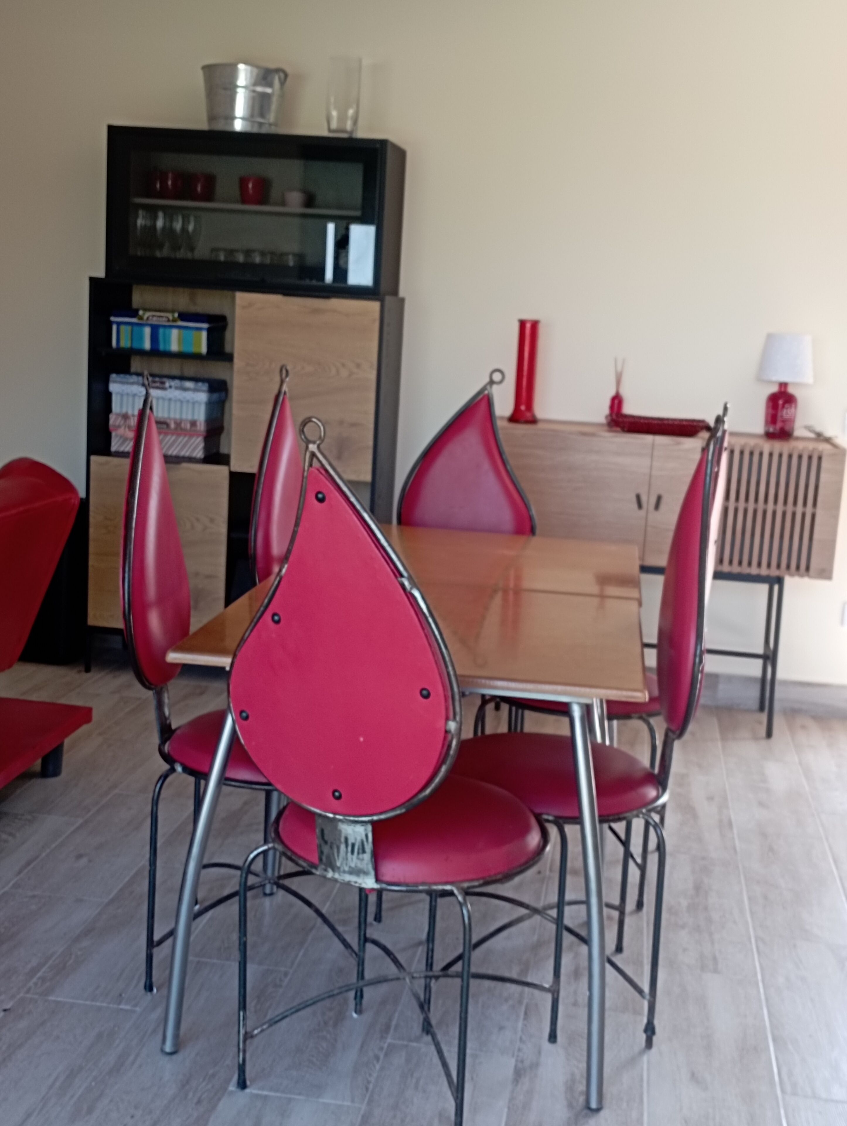 Un comedor con una mesa de madera y cuatro sillas rojas. En el fondo, un armario negro con puertas de vidrio.